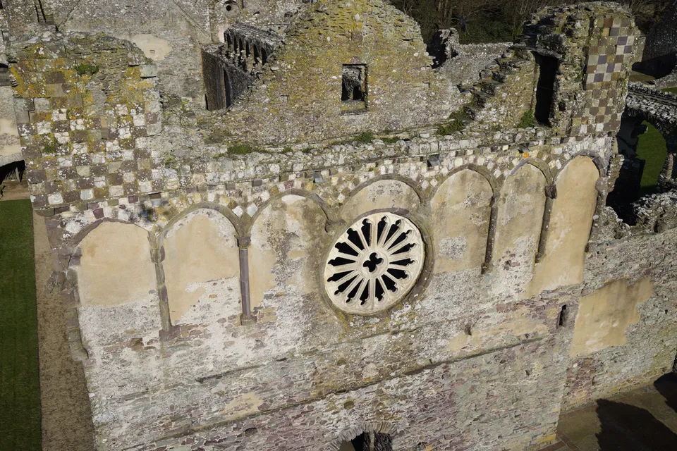 Aerial photograph looking across the roofless nave and surrounding ruined walls of a bishop's palace.