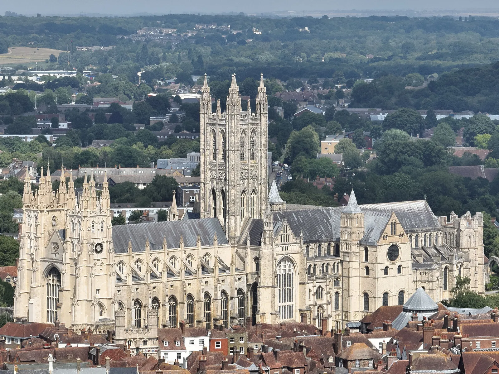 Aerial photograph of a large Gothic cathedral with a tall central tower and two western towers, surrounded by tiled roofs and trees.