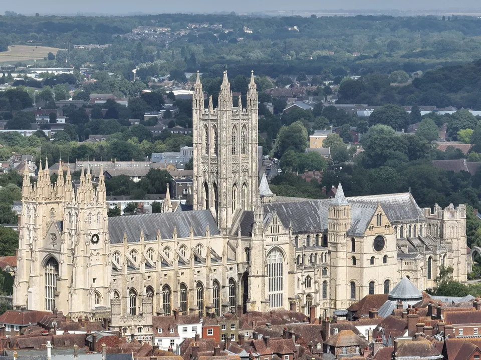 Aerial photograph of a large Gothic cathedral with a tall central tower and two western towers, surrounded by tiled roofs and trees.