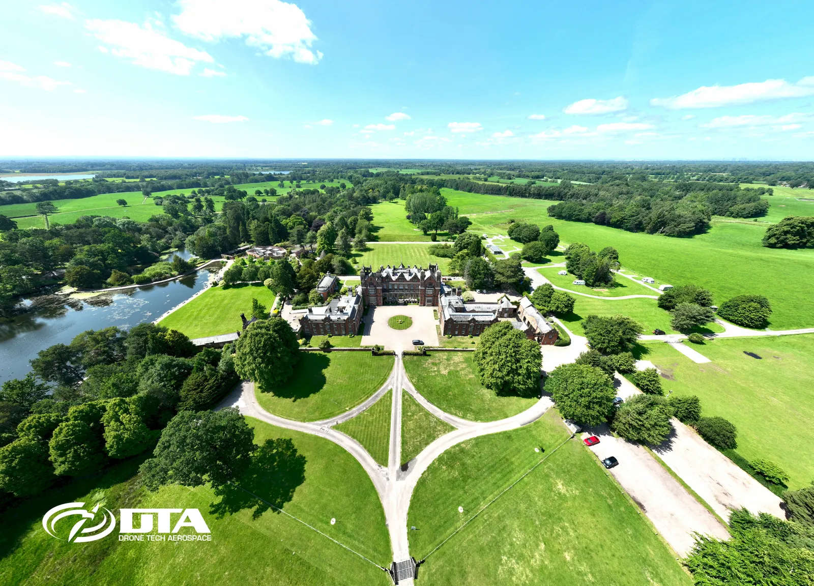 Aerial photograph of a large country house facade with formal gardens and driveway.