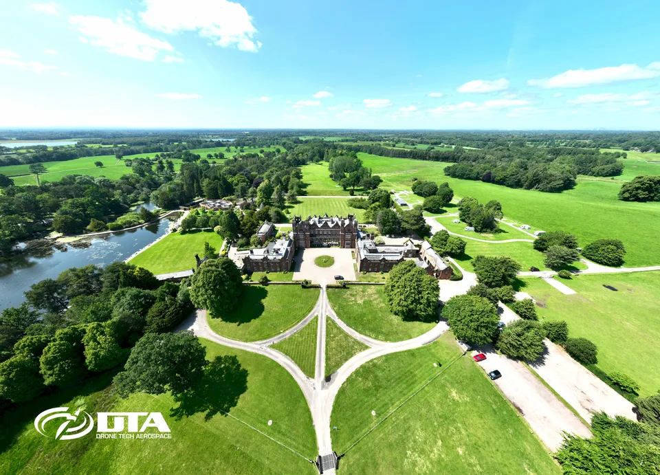 Aerial photograph of a large country house facade with formal gardens and driveway.