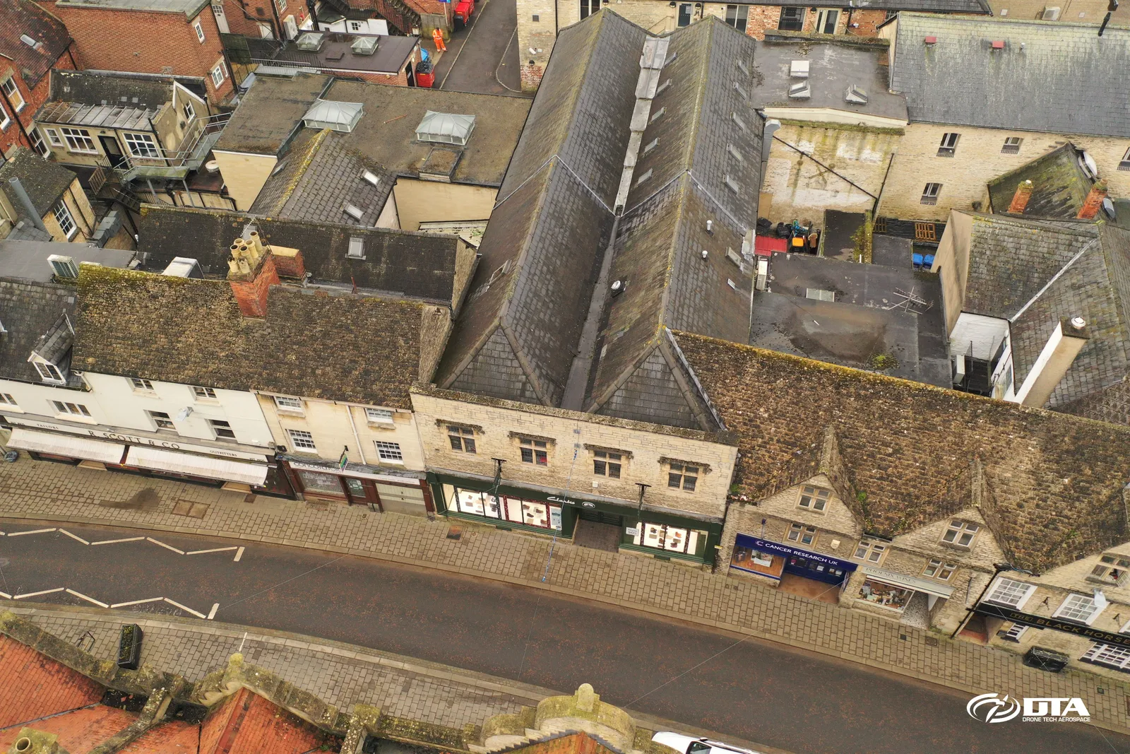 Angled aerial photograph of period buildings and rooftops along a historic town-centre street in Cirencester.