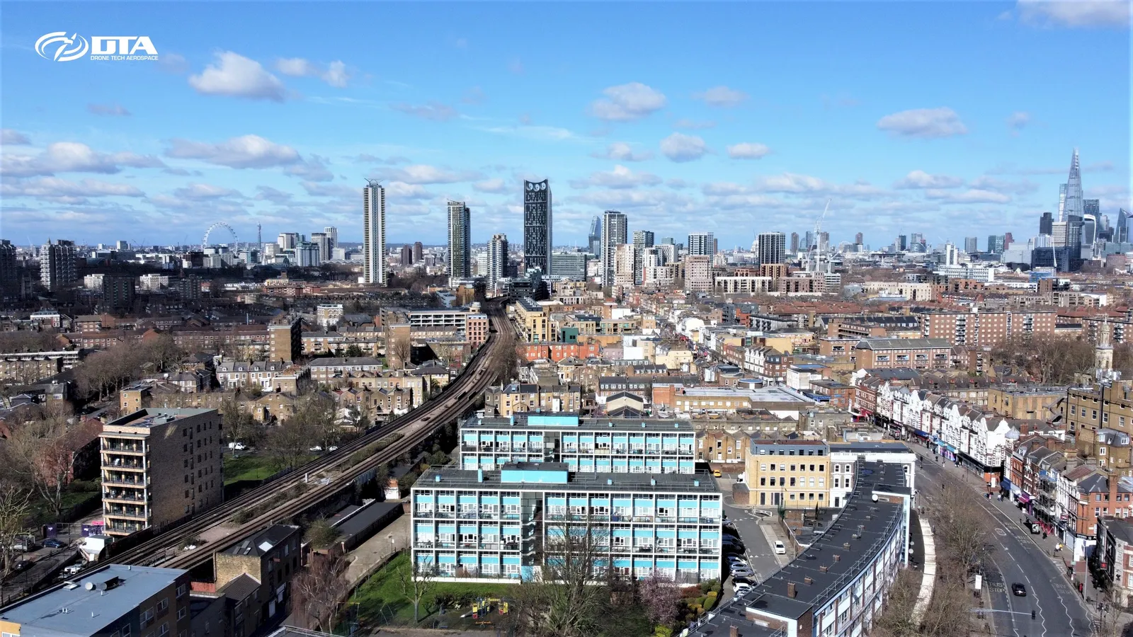 Aerial drone photograph looking across the central London skyline with high-rise towers and rooftops beneath a hazy sky.