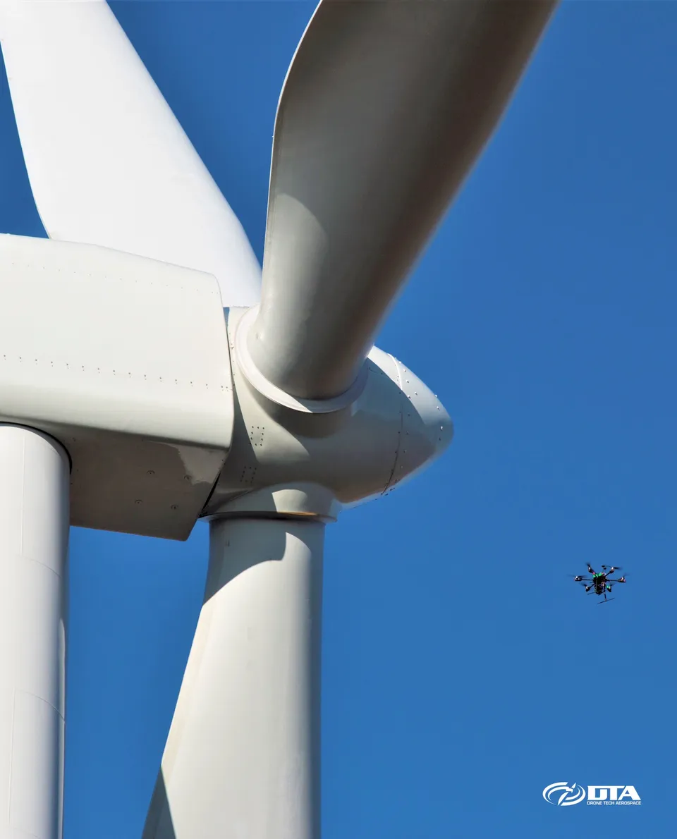 Vertical aerial photograph looking up the length of a wind turbine tower and blade during an inspection flight.