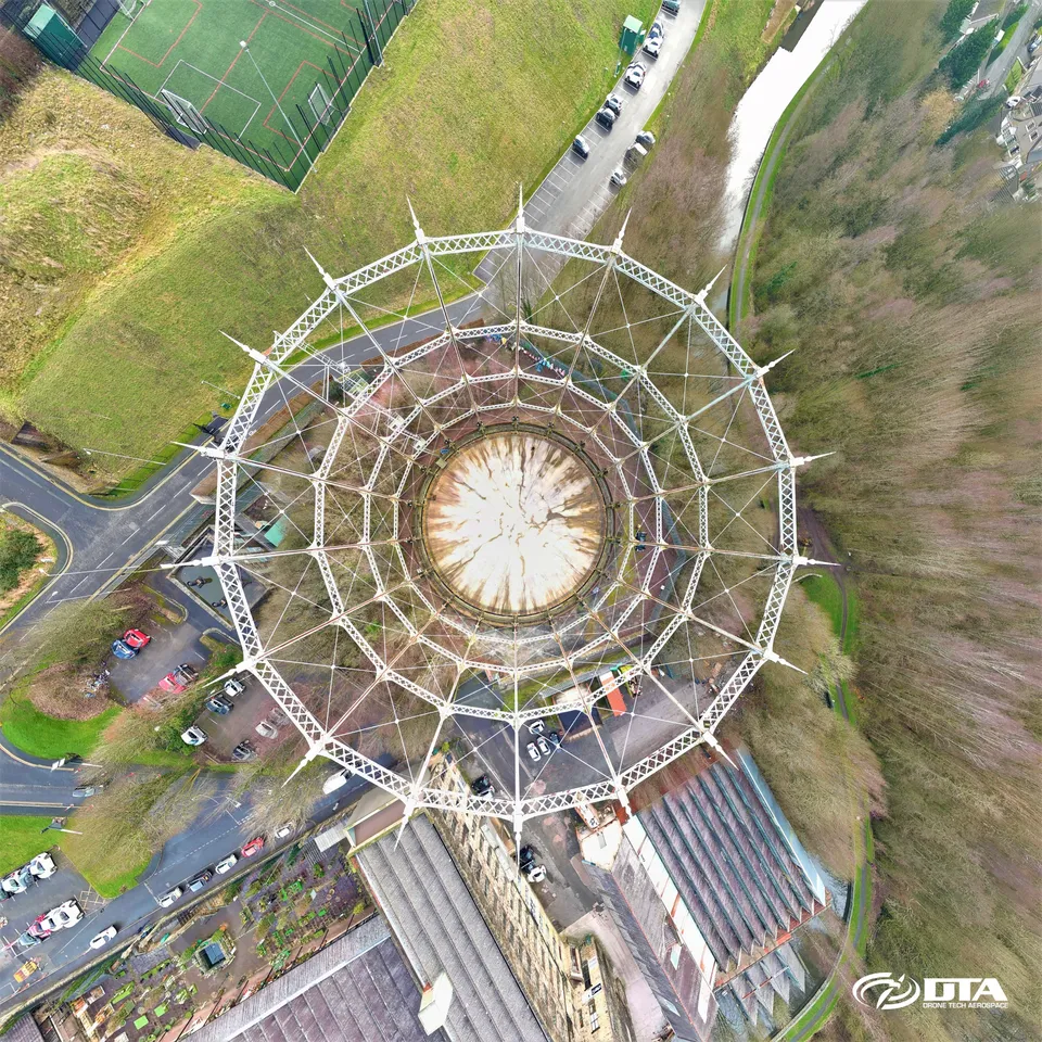 Wide panoramic aerial photograph of a large cylindrical gas holder structure and surrounding site.