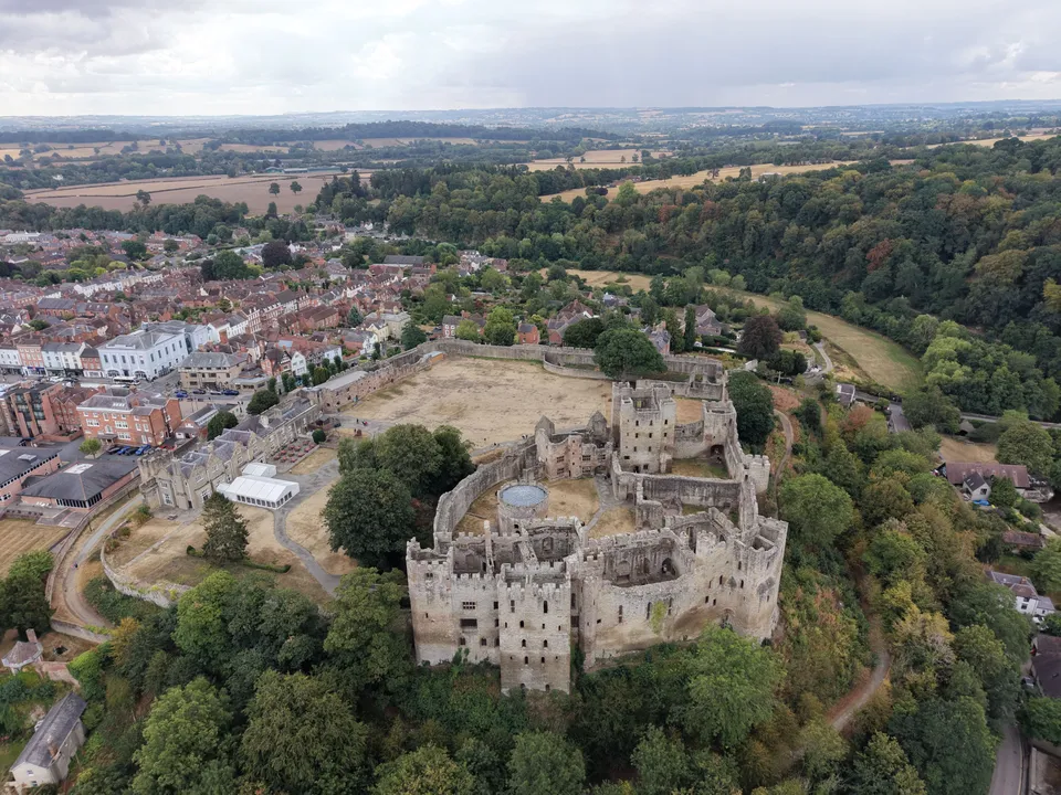 Ludlow Castle and its outer bailey seen from the drone, with the town beyond and the River Teme woodland to the right.