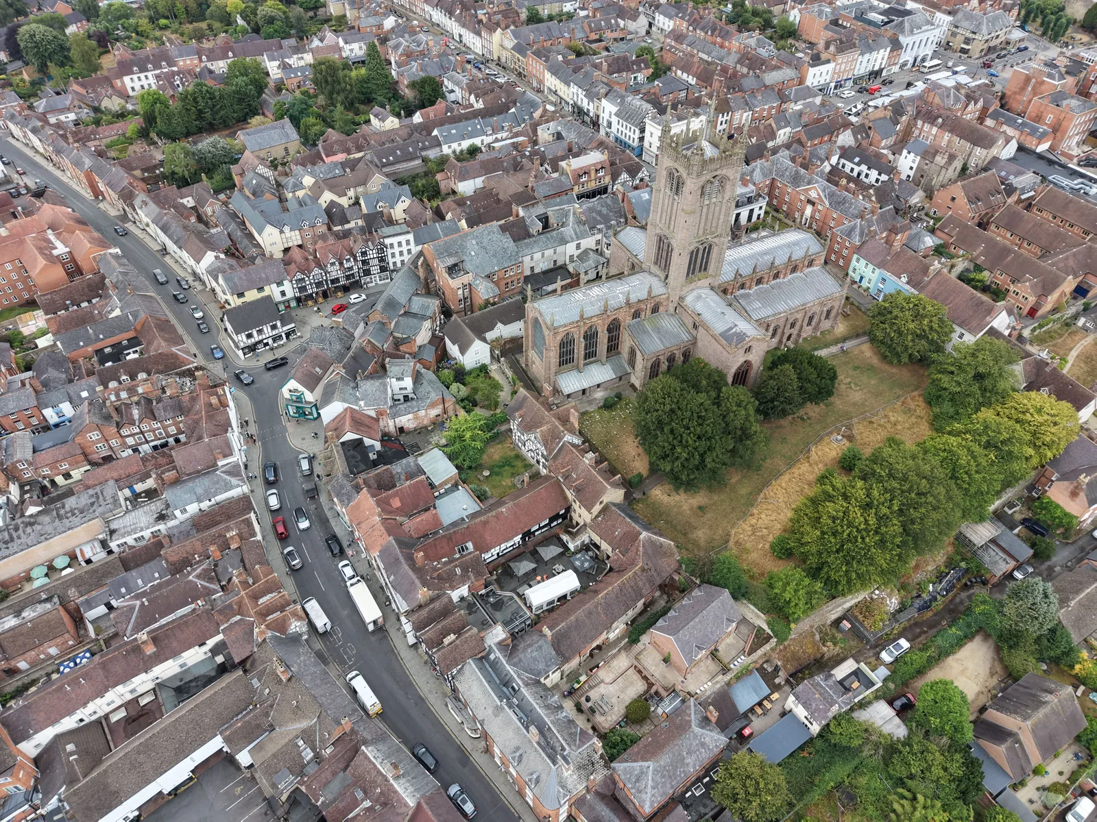 Aerial view of a large parish church with a tall tower set among the tiled roofs and narrow streets of a historic market town.