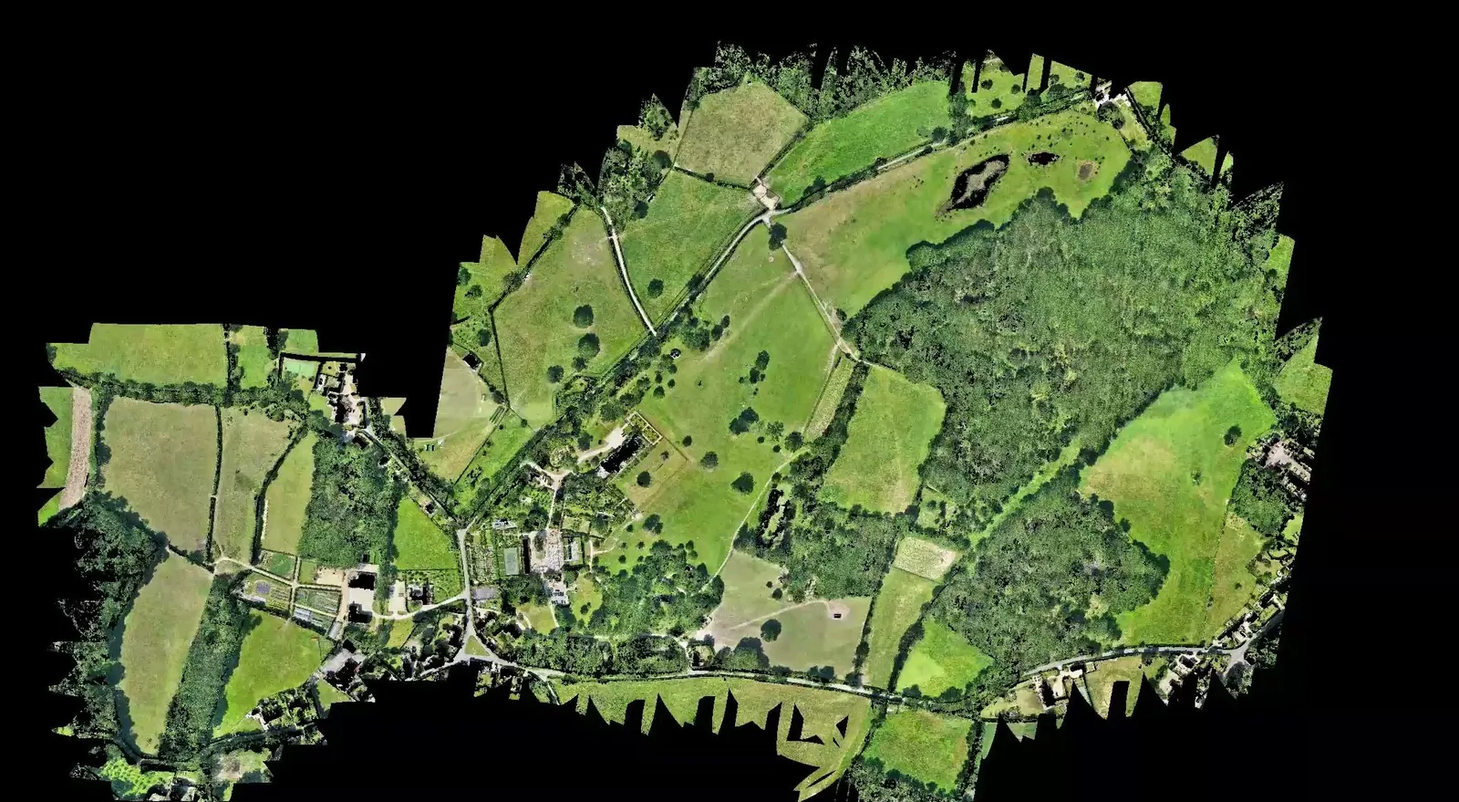 Aerial orthomosaic map of a large rural estate showing fields, woodland, gardens, ponds and buildings against a black background.