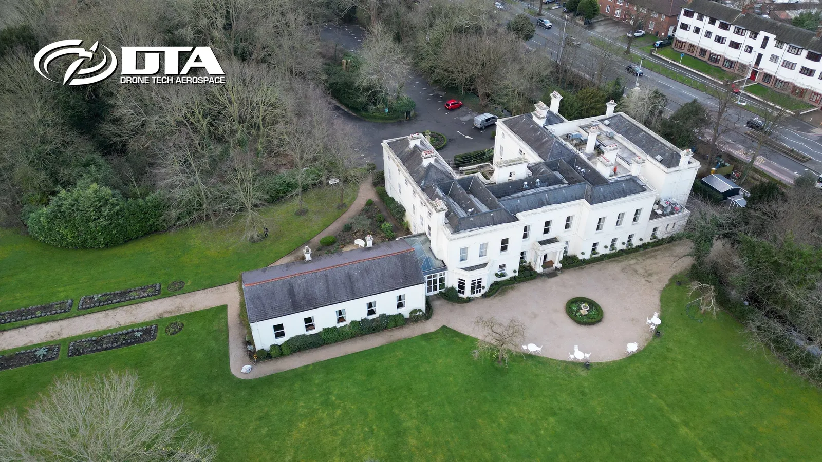 Aerial photograph of a country house set within a park with mature trees and a river.