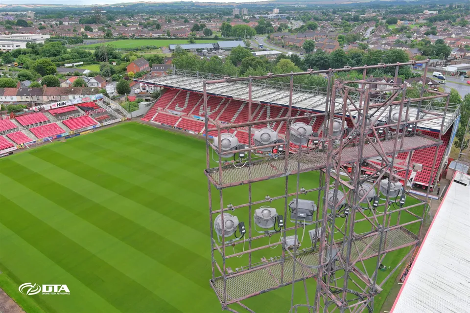 Aerial photograph looking up at a tall stadium floodlight tower against the sky.