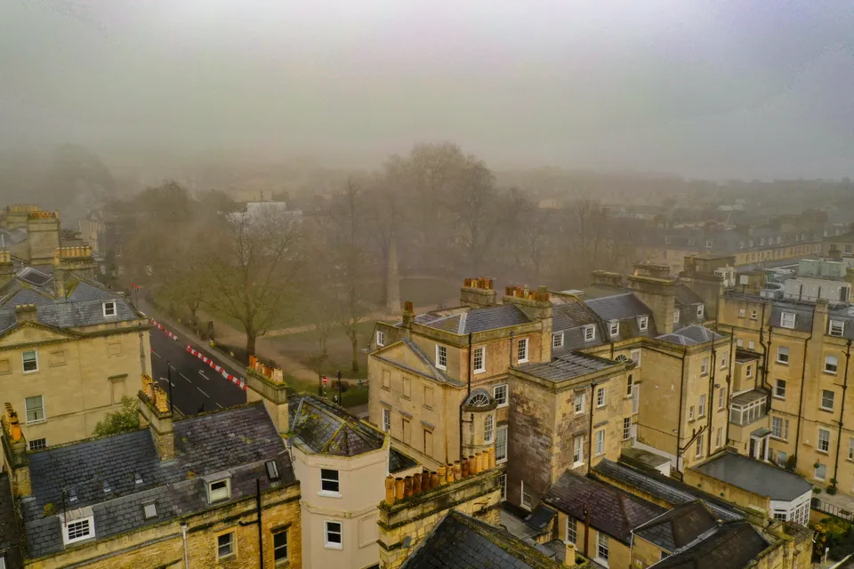 Foggy aerial view of Bath's Georgian rooftops and chimneys overlooking Queen Square with the 1738 Beau Nash Obelisk